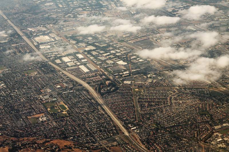 An aerial view of Milpitas, low buildings and streets laid out below the East Bay hills.