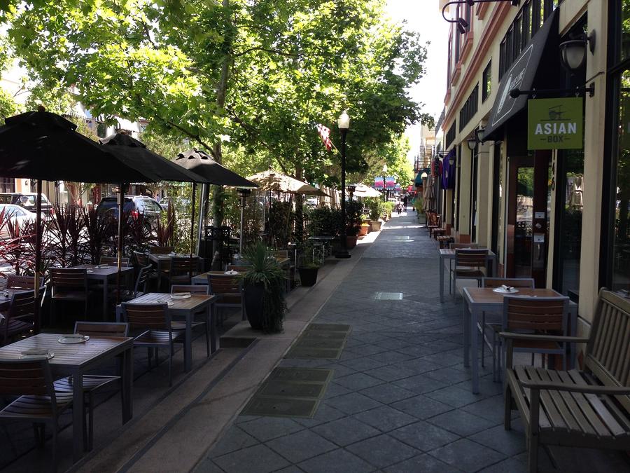 The sidewalk on Castro Street in Mountain View, restaurant tables set out under umbrellas along a tree-shaded street.