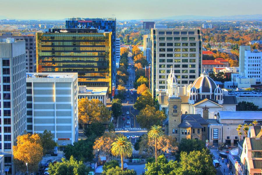 Downtown San Jose seen from above on a clear day, office towers and the cathedral dome among trees turning autumn colours.